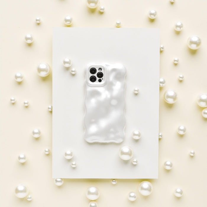 A Coconut Lane 3D Pearl Phone Case in white, featuring a glossy, wavy, pearl effect, is placed on a white rectangular sheet. The sheet is surrounded by various sizes of white pearls scattered on a light beige surface, creating an elegant and sophisticated display.