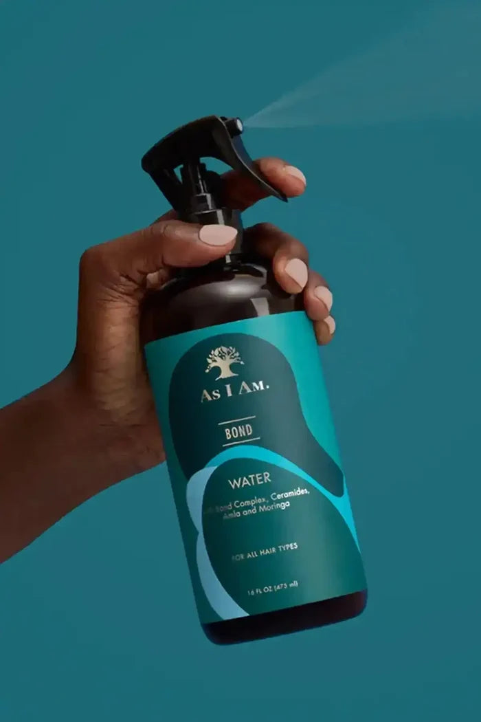 Hand holding As I Am Bond Water spraying a fine mist, ideal for daily hair refresh and reviving curls and coils.
