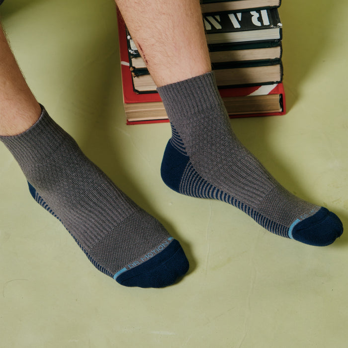 Gray and navy quarter compression socks with ribbed cuffs and striped design, worn on feet resting on a surface.
