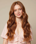 Woman with long wavy red hair extensions wearing a pink top against a beige background