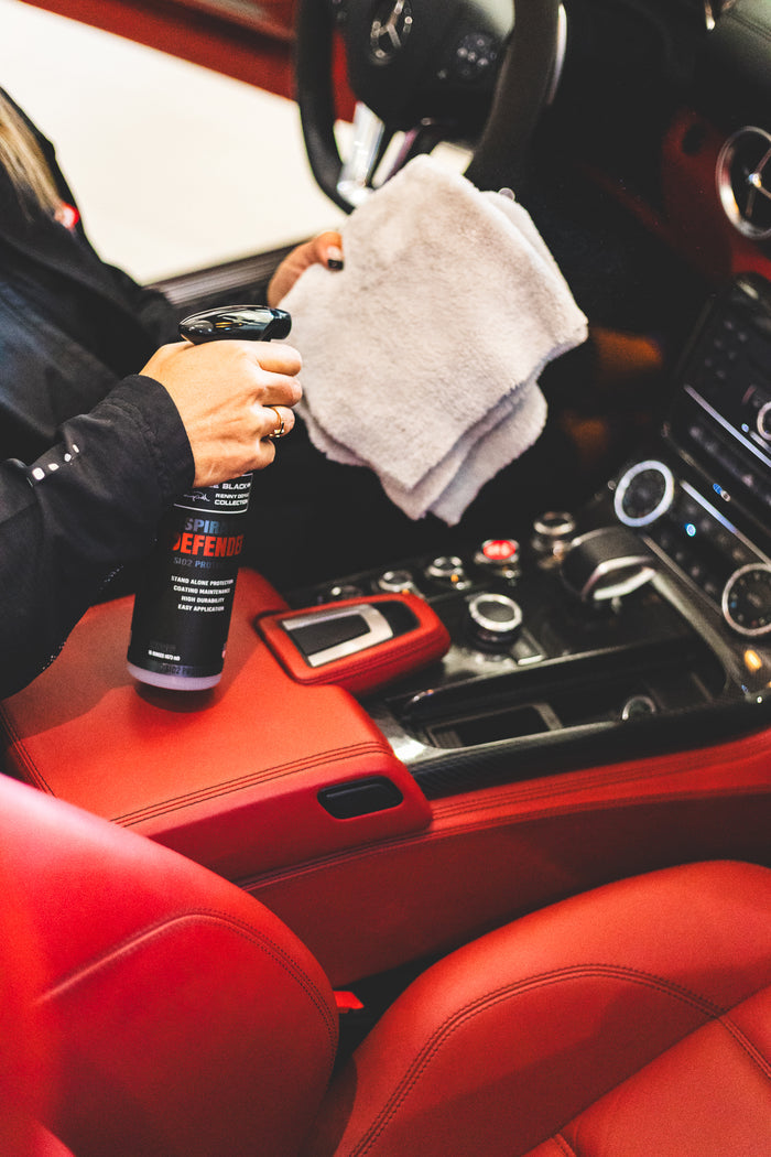 A person spraying an Ice Grey microfiber towel with P&S Inspiration Defender.