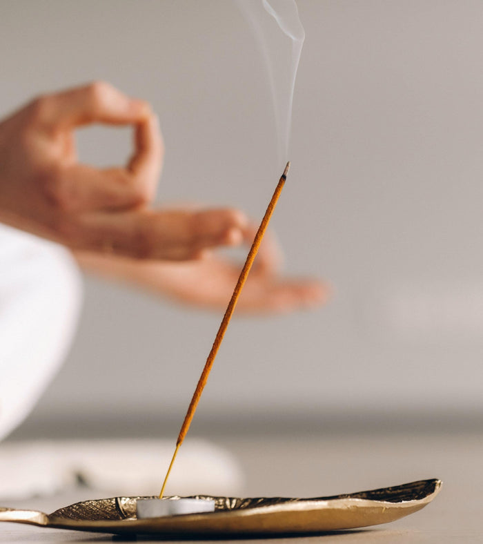 Burning agarbatti incense stick releasing smoke over a small metal holder