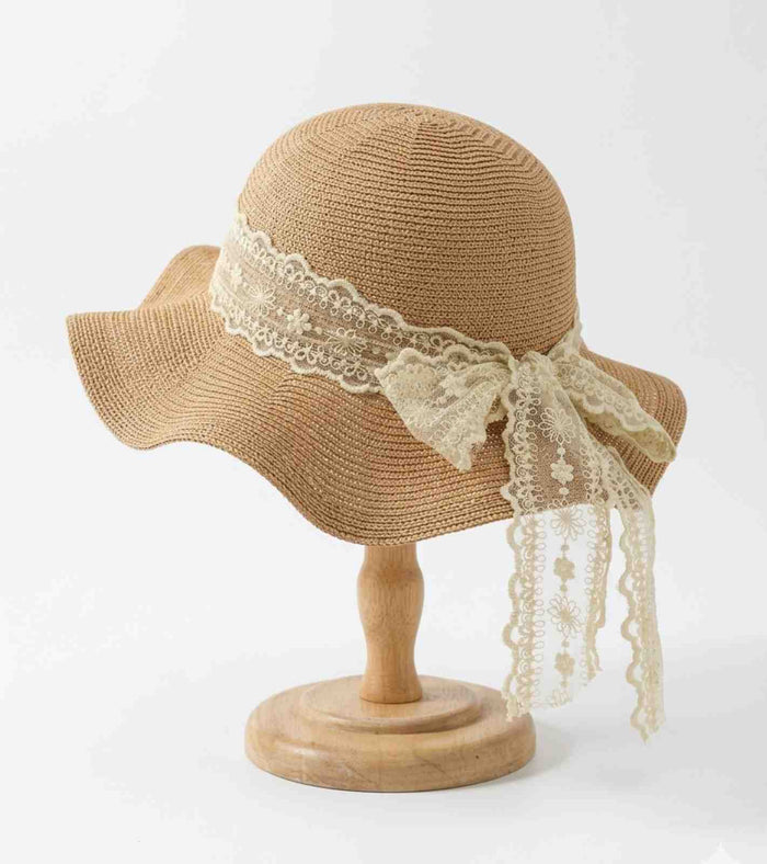 Sand straw wide-brim sun hat with lace band and tied ribbon tails on stand