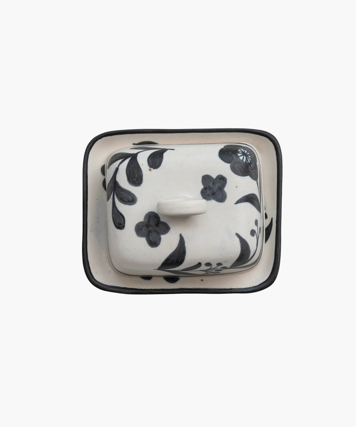 An overhead picture of a ceramic butter dish with a lid featuring black floral designs and a circular handle, set against a plain white background. The tone is elegant and artistic. | Wildwood Home Co.