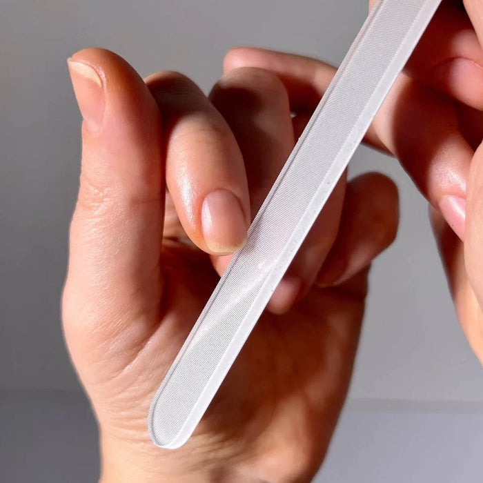 Hand holding a glass nail file against a neutral background.