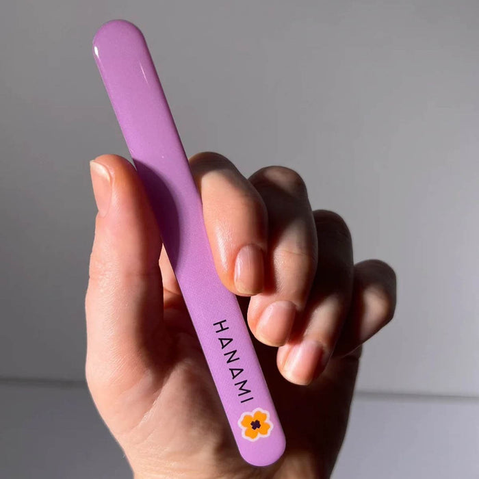 Hand holding a purple glass nail file with 'HANAMI' branding against a neutral background.