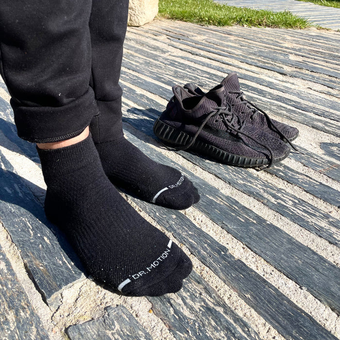 Black quarter compression socks are worn with black athletic shoes on a textured surface.