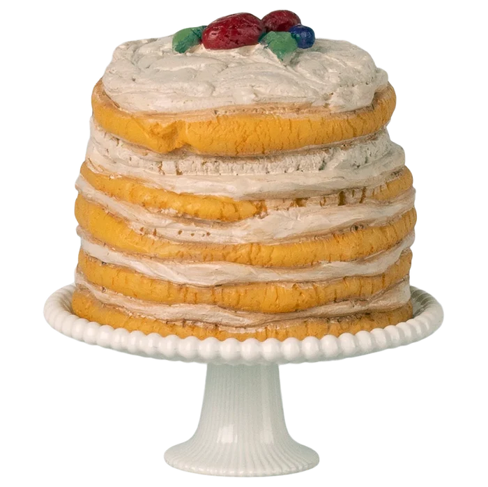 Layered cake with white frosting and fruit on top, placed on a white cake stand.