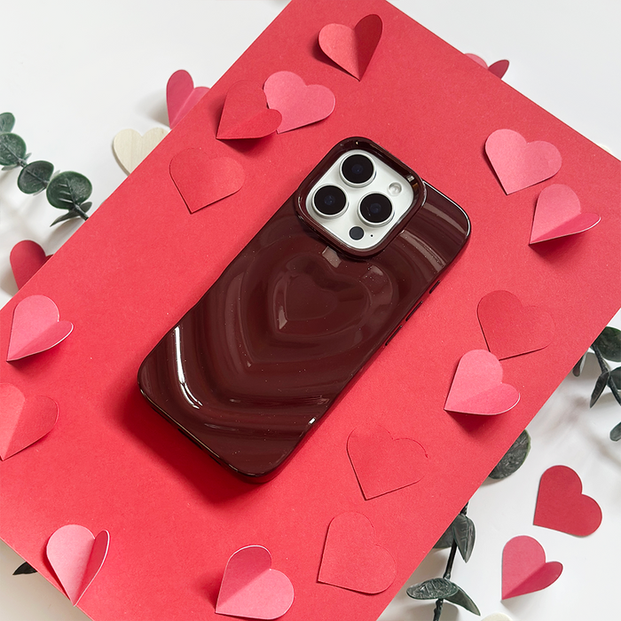 Burgundy Coconut Lane Melting Heart phone case on a red card, surrounded by paper hearts and green sprigs.