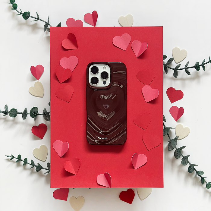 Burgundy Coconut Lane Melting Heart phone case on red paper with paper hearts and green leaves.