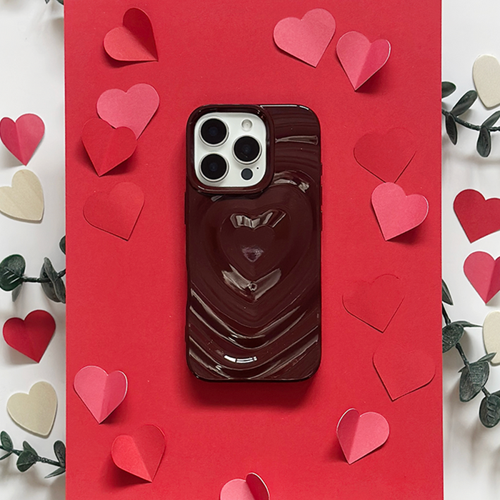 Burgundy Coconut Lane Melting Heart phone case on red paper, with paper hearts and green leaves around it.
