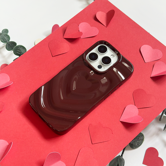Burgundy Coconut Lane Melting Heart phone case on a red background with pink and red paper hearts.