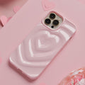 A Coconut Lane Melting Heart Phone Case in Peony Pink encases a smartphone resting on a pink surface. Multiple paper hearts are scattered around, enhancing the romantic and playful theme. The background features an array of pink shades and textures.
