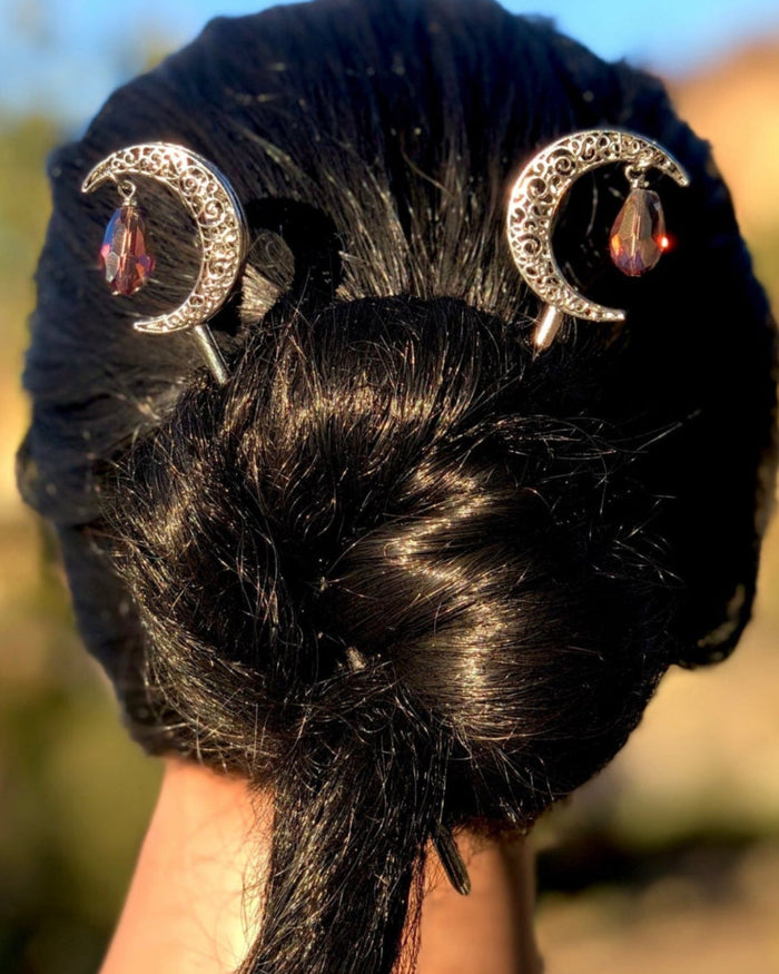 Silver crescent moon hair sticks with red crystal gemstone dangles securing a twisted bun, shown from the back to display the celestial moon design and elegant hairstyle.