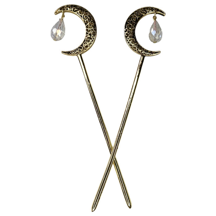 Pair of antique gold crescent moon hair sticks with clear crystal teardrop dangles, shown crossed on a white background to display the front view and celestial moon design.