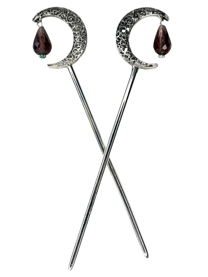 Pair of silver crescent moon hair sticks with purple crystal teardrop dangles, shown crossed on a white background to display the front view and celestial moon design.