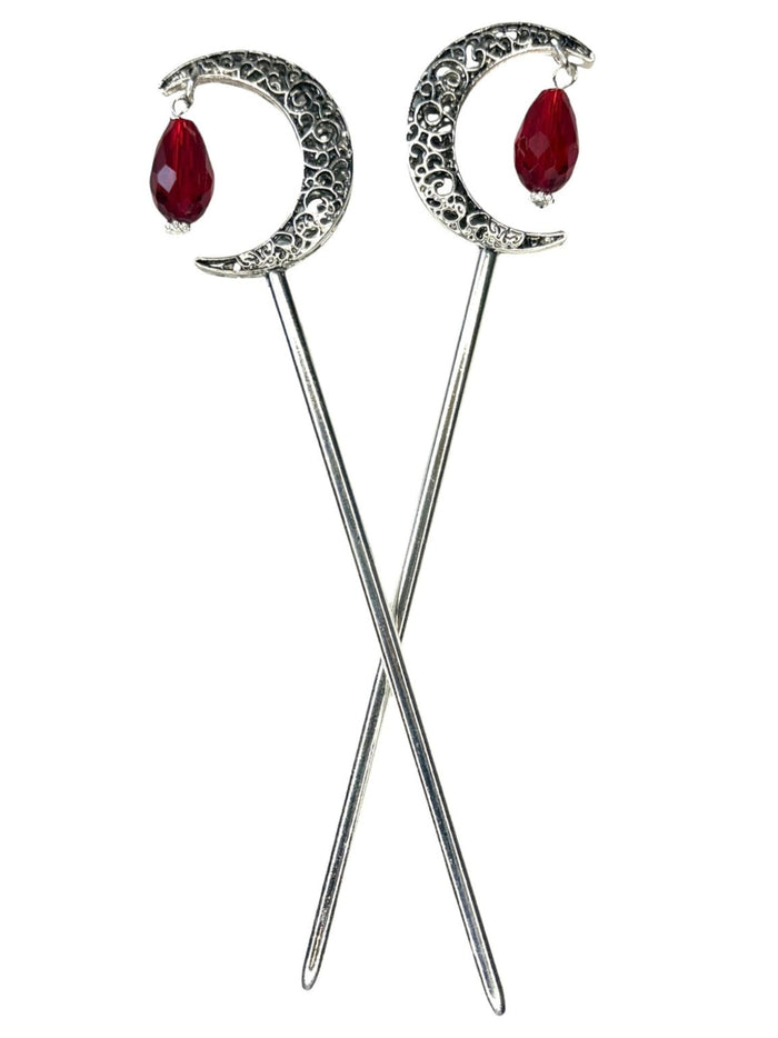 Pair of silver crescent moon hair sticks with red crystal teardrop dangles, shown crossed on a white background to display the front view and celestial moon design.