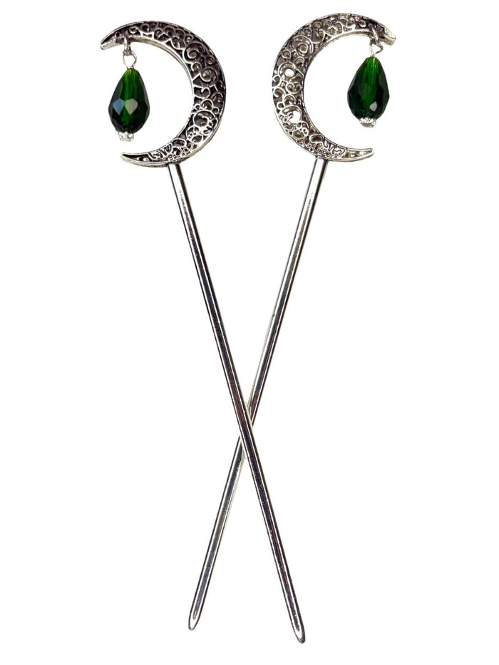 Pair of silver crescent moon hair sticks with green crystal teardrop dangles, shown crossed on a white background to display the front view and celestial moon design.