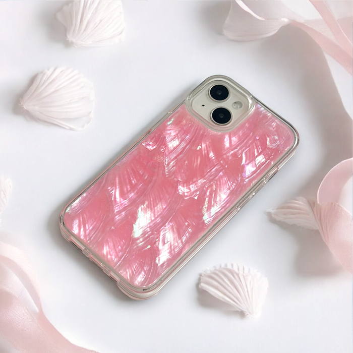 Pink natural shell phone case by Coconut Lane on a white surface, surrounded by ribbons and seashells.