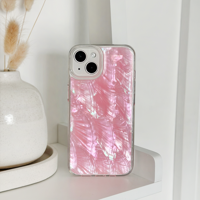 Pink natural shell phone case on a white shelf beside a white vase with dried grass.
