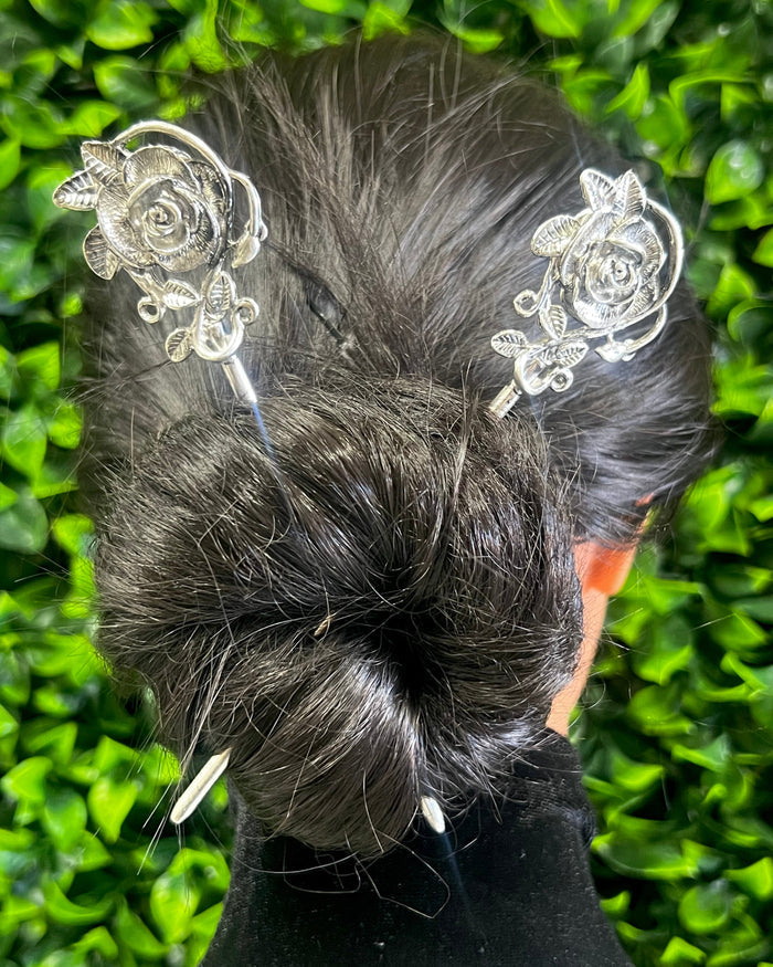 Model wearing silver rose hair sticks securing a bun hairstyle, elegant floral metal hair accessories for weddings, festivals, Renaissance fairs, and everyday wear.