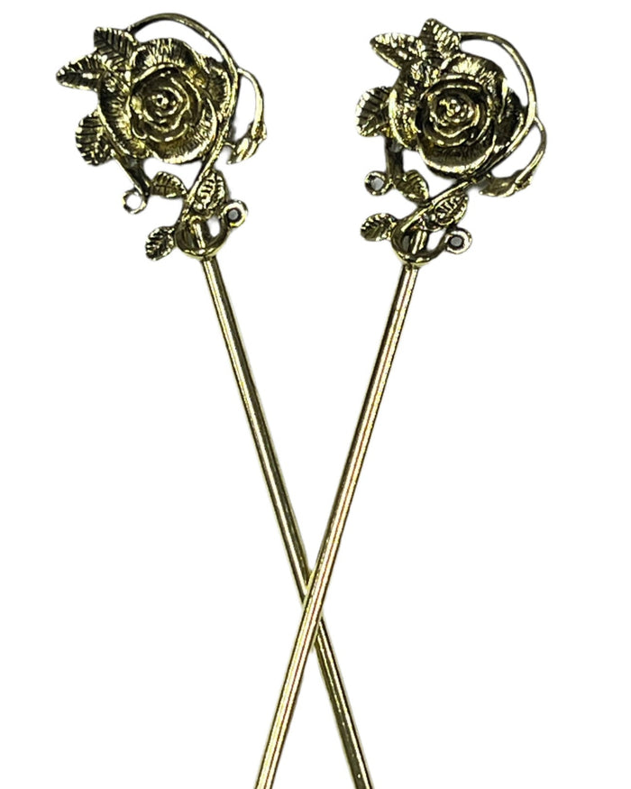 Pair of gold rose hair sticks with floral vine design, decorative metal hair pins crossed on a white background for buns, updos, and elegant hairstyles.