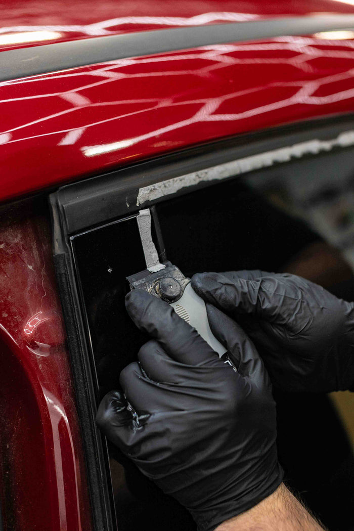 Person using a KochChemie Scraper tool on a car window of a red vehicle.