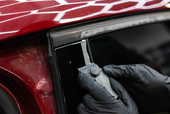 Person using a KochChemie Scraper tool on a car window of a red vehicle.