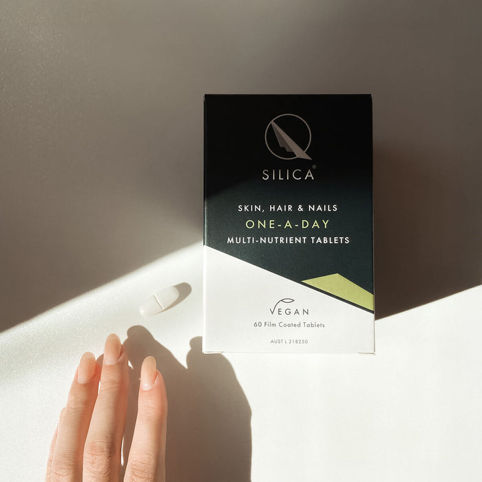 Qsilica Skin, Hair & Nails supplement box on a neutral background with a hand and a tablet.