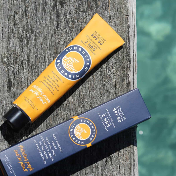 SunButter Skincare Sunscreen 120g yellow tube next to blue packaging on a wooden surface next to the sea.
